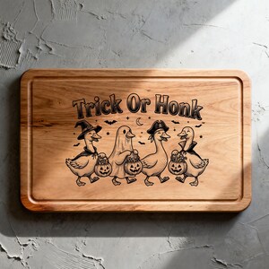 May include: A rectangular wooden cutting board featuring a laser-engraved illustration of four ducks in Halloween costumes, including a witch, a ghost, and a pirate, holding jack-o'-lantern buckets, with the text Trick Or Honk above them.