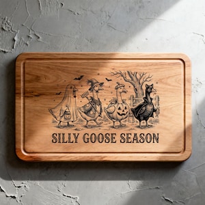 May include: A rectangular wooden cutting board with a grooved border featuring a black engraved illustration of four geese in Halloween costumes. The text SILLY GOOSE SEASON is printed below the geese, which include a ghost, a farmer, a pumpkin, and a vampire.