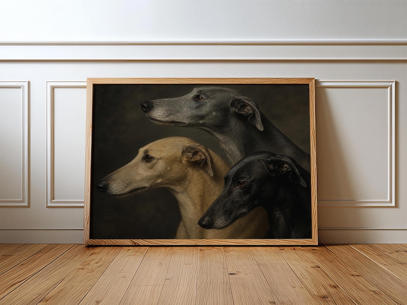 May include: A framed print featuring three greyhound dogs in profile. The dogs are depicted in shades of grey, tan, and black against a dark background. The artwork is displayed in a wooden frame, leaning against a white wall and wooden floor.
