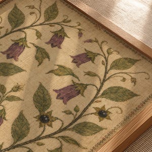 May include: A framed rectangular wall art piece featuring a beige linen-textured background with a botanical illustration of trailing green vines, dark green leaves, small black berries, and purple bell-shaped flowers encased in a light wood frame.