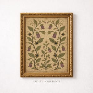 May include: A framed wall art print featuring a symmetrical botanical illustration of purple bell-shaped flowers and green leaves on a textured beige background. The artwork is enclosed in an ornate, metallic gold-toned rectangular frame.