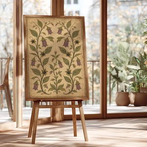 May include: A rectangular framed artwork featuring a symmetrical botanical illustration on a textured beige background. The design displays green leafy vines with purple bell-shaped flowers and small dark berries, all enclosed in a wooden frame.