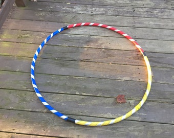 Könnte beinhalten: Ein bunter Hula-Hoop mit roten, weißen, blauen und gelben Streifen. Der Reifen liegt auf einem Holzdeck.