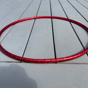 Puede incluir: Un aro de ejercicio rojo con un acabado brillante. El aro está sobre una superficie de madera gris.