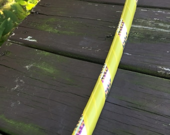 May include: A yellow hoop with a black and white patterned tape design. The hoop is lying on a wooden surface.