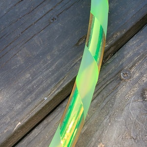 May include: A green and gold hoop with a frosted finish. The hoop is made of plastic and has a shiny, iridescent finish.
