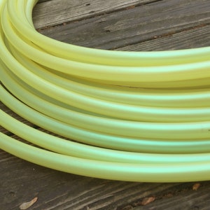 May include: A close-up of a stack of yellow iridescent hula hoops. The hoops are made of a smooth, shiny plastic and have a slight shimmer to them.