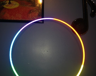 May include: A colorful LED hoop with green, yellow, and white lights. The hoop is lit up and is in focus against a blue wall.