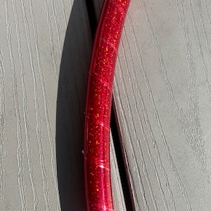 Puede incluir: Primer plano de un aro rojo con purpurina, que muestra la textura de la purpurina y el color rojo.