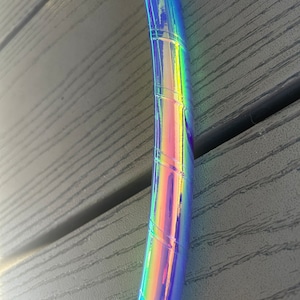 May include: Close-up of a blue iridescent hoop with a rainbow sheen. The hoop is made of plastic and has a smooth, shiny finish.