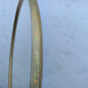 May include: A gold hoop with iridescent glitter embedded in the plastic. The hoop is partially visible against a white background.