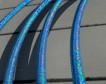 May include: Three blue iridescent glitter hula hoops stacked on top of each other. The hoops are on a grey wooden surface.