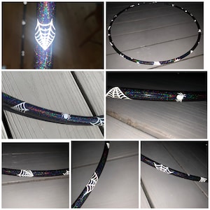 May include: A black and iridescent hoop with white spiderwebs and spiders painted on it. The hoop is lying on a wooden surface.