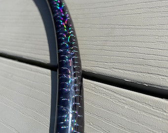 Può includere: Un cerchio nero con nastro olografico iridescente. Il nastro ha un motivo arcobaleno con colori verde, blu, viola e rosso.