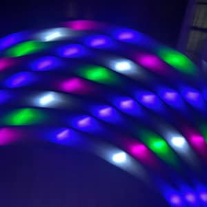 May include: A close-up of a string of LED lights with blue, green, white, and pink lights. The lights are arranged in a curved pattern, creating a dynamic and colorful display.