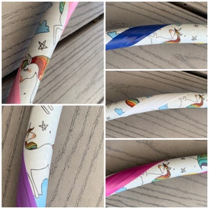 May include: Close-up of a white hoop with a unicorn and rainbow design. The hoop is wrapped with different colored tapes, including pink, purple, blue, and white.