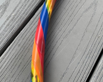 May include: A colourful hoop with blue, red, yellow and gold stripes. The hoop is made of plastic and is lying on a grey wooden surface.