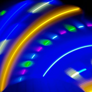 May include: Abstract image with a blue background and colorful streaks of light. The streaks of light are yellow, green, white, and pink. The image is reminiscent of a night sky with fireworks.