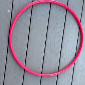 May include: A circular hula hoop in a vibrant, solid neon pink color. The hoop features a smooth, continuous plastic surface with a consistent tubular thickness throughout its entire circumference, forming a perfect circle shape for physical activity.