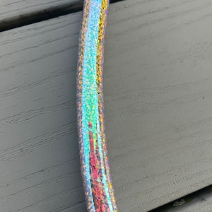 Puede incluir: Primer plano de un aro plateado iridiscente con una cinta de purpurina azul. El aro es de plástico y tiene un acabado brillante.