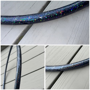 Puede incluir: Un aro negro con purpurina iridiscente incrustada en el plástico. El aro está sobre una superficie de madera.