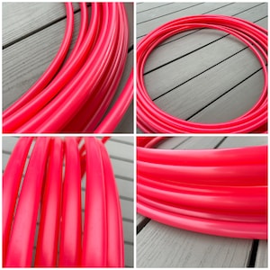 Puede incluir: Primer plano de un aro de hula de plástico rojo brillante. El aro está hecho de múltiples capas de tubos de plástico, creando un efecto vibrante y colorido.