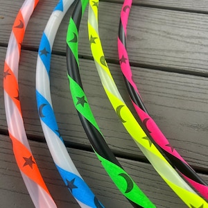 May include: Five colorful plastic hula hoops with black stars and crescent moons printed on them. The hoops are arranged in a row, with the orange hoop at the bottom and the pink hoop at the top.