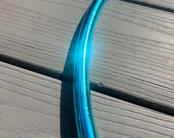 May include: A section of a bright blue, metallic hula hoop. The hoop is curved and reflects light, creating a glowing effect. The background is a weathered, grey wooden surface.