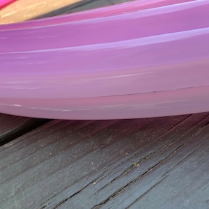 May include: A close-up of a pink and purple object with a curved shape. The object appears to be made of a translucent material, with a smooth surface. The object is resting on a dark wooden surface.