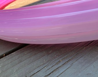 Puede incluir: Primer plano de un objeto curvo rosa y morado. El objeto está hecho de un material translúcido con una superficie lisa. Descansa sobre una superficie de madera oscura. Los colores se funden del rosa al morado.
