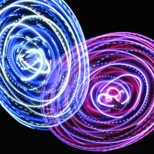 May include: Two swirling circles of light, one blue and white, the other pink and purple, against a black background.
