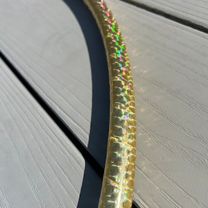 May include: A gold hoop with a green and iridescent finish. The hoop is made of plastic and has a smooth surface.