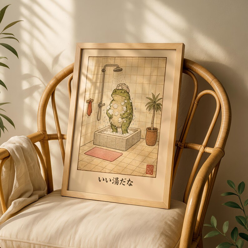 May include: A framed print featuring a whimsical illustration of a frog taking a shower. The frog is in a bathtub, covered in bubbles, with a showerhead above. The print is in a light wood frame and includes Japanese text.