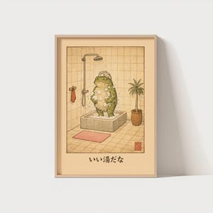 May include: A framed print featuring a green frog taking a shower in a stone tub. The frog wears a shower cap and is surrounded by bubbles. The bathroom has a shower head, a towel, a small rug, and a potted plant. The Japanese text "いい湯だな" is at the bottom.