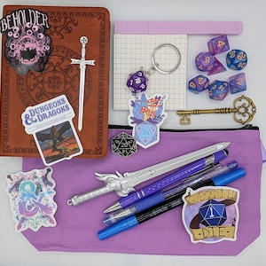 May include: A collection of fantasy role-playing game accessories, including dice, pens, stickers, a key, and a notebook. The items are arranged on a purple pouch and a brown leather-bound journal. Stickers include the text "BEHOLDER" and "DUNGEONS & DRAGONS".