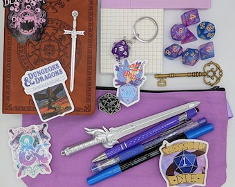 May include: A collection of fantasy role-playing game accessories, including dice, pens, stickers, a key, and a notebook. The items are arranged on a purple pouch and a brown leather-bound journal. Stickers include the text "BEHOLDER" and "DUNGEONS & DRAGONS".