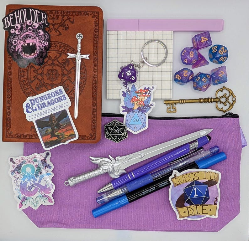 May include: A selection of fantasy role-playing game accessories, including dice, pens, stickers, a key, and a notebook. The items are arranged on a purple pouch and a brown leather-bound journal. Stickers include the text "BEHOLDER" and "DUNGEONS & DRAGONS".