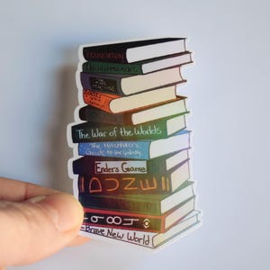 May include: A sticker featuring a stack of books with titles like "Foundation," "The War of the Worlds," and "Ender's Game." The books are in various colors, with titles written in a handwritten style. The sticker has a white border.