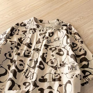 May include: A cream-coloured short-sleeve button-down shirt featuring an all-over black graphic print of various panda bears in different poses. The shirt includes a chest pocket and the text "BLACK AND WHITE" and "Great things are" printed.