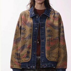 May include: A denim jacket with a brown and blue patterned design. The jacket has a dark blue denim collar, cuffs, and pockets. The jacket has a button-up front and two front pockets. A brown baseball cap is worn.