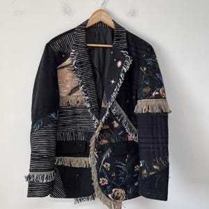 May include: A patchwork blazer featuring a mix of black, white, and multi-colored fabrics. The garment includes panels with horizontal stripes, floral patterns, and celestial motifs, accented with frayed edges, notched lapels, and two front pockets.