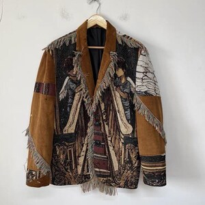 May include: A brown corduroy blazer with a tapestry design featuring figures and architectural elements. The jacket has a fringed trim and a contrasting black lining. The sleeves are a solid brown corduroy.
