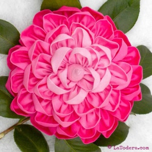 May include: A large, pink fabric flower with a layered, ruffled design. The flower is made of two shades of pink, with a darker pink outer layer and a lighter pink inner layer.
