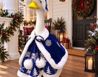 May include: A white goose statue wearing a blue velvet cape and matching bonnet with white faux fur trim. The cape features a white snowflake pattern, white lace detailing, and two white pom-poms. A silver snowflake brooch is pinned to the cape.