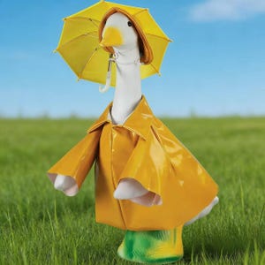 May include: A whimsical goose statue wearing a bright yellow raincoat and matching umbrella. The goose has a white body, yellow beak, and green boots, standing in a grassy field under a blue sky. A charming decorative item for a garden or patio.