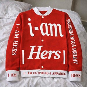 May include: Red and white varsity jacket with the text "i-am Hers" in large white letters. The sleeves have the text "I. AM HERS" and "AFFIRM YOUR PERSONA". The bottom of the jacket reads "I-AM CLOTHING & APPAREL".