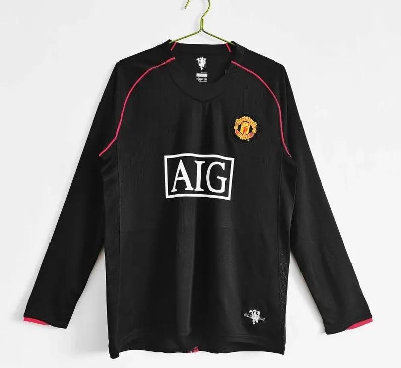 May include: Black long-sleeved football shirt with red trim and accents. The shirt displays the AIG logo in white, a team crest, and a small emblem. The shirt is hanging on a gold hanger.