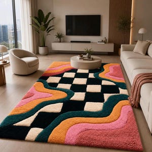 May include: A rectangular area rug featuring a central black and cream checkered pattern surrounded by wavy, flowing bands of orange, pink, and dark teal. The rug has a thick, textured pile and covers a large portion of the light-coloured floor.
