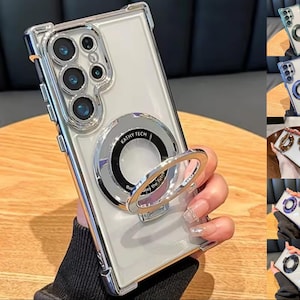 Könnte beinhalten: Transparente Handyhülle mit silbernem Metallringhalter. Die Hülle hat eine transparente Rückseite und einen silbernen Rahmen. Der Ringhalter trägt den Text "KATHY TECH" und "qual the future". Die Hülle hat einen Objektivschutz.