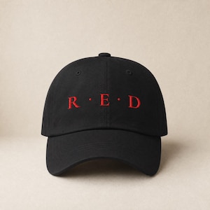 Könnte beinhalten: Schwarze Baseballkappe mit dem Wort "RED" in roter Schrift auf der Vorderseite gestickt. Die Kappe hat einen gebogenen Schirm und eine runde Krone. Der Text ist zentriert und gleichmäßig angeordnet.